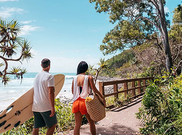 Couple with surfboards walking to Noosa beach